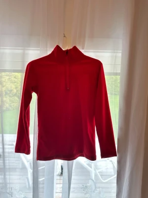 Röd fleece tröja med halv dragkedja - Mysig röd fleece tröja med hög krage och halv dragkedja framtill. Långärmad modell som passar perfekt när du vill hålla dig varm. Enkel och stilren design utan synliga loggor eller mönster.