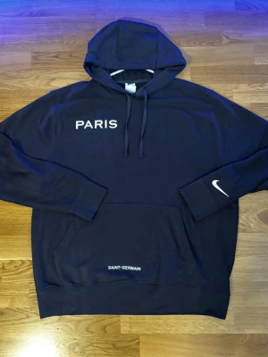 Nike PSG hoodie (mörkblå) HELT NY! - Helt ny oanvänd snygg mörkblå hoodie från Nike med texten PARIS på bröstet, swoosh på ärmen och SAINT-GERMAIN vid fickan. Klassisk huva med dragsko och Nike-logga på ärmen. Aldrig använd, köpt från Nike.com.