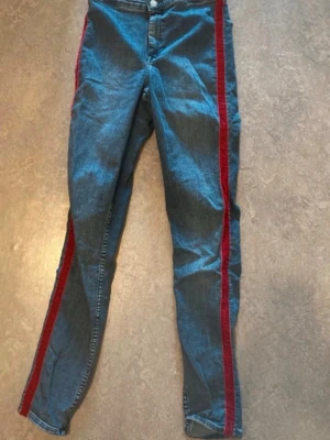 Blå jeans med röd revär - Snygga blå jeans med raka ben och en röd revär längs båda sidorna. Klassisk femficksmodell med knapp och dragkedja framtill. Jeansen har en streetstil och är tillverkade i denim.