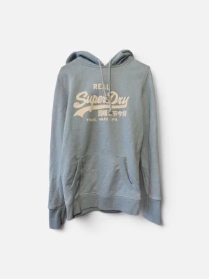 Ljusblå hoodie från Superdry - Ljusblå hoodie från Superdry med vit logga och text på bröstet. Klassisk känguruficka framtill, justerbar dragsko i huvan och ribbade muddar vid ärmar och nederkant. Perfekt för en avslappnad och cool stil. Den vita texten har börjat försvinna lite 