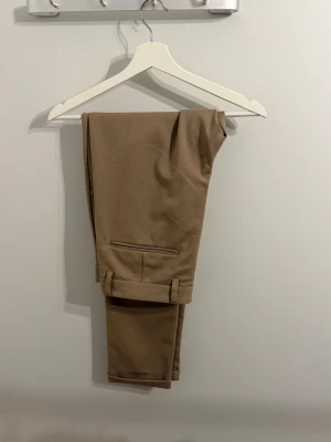 Beige kostymbyxor Lindbergh’s - Snygga beige chinos från Lindbergh med klassisk passform. Byxorna har framfickor, bälteshällor och en enkel bakficka med diskret söm. Tillverkade i ett mjukt och bekvämt bomullsmaterial. Köpt för 1100kr
