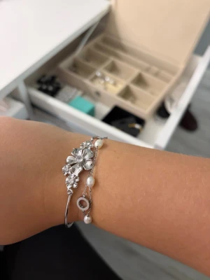 ioaku armabnd  - Snyggt armband från ioaku med detaljerade blommor i mitten och små kristaller. De är helt nytt och aldrig använt. Nypris är 600kr