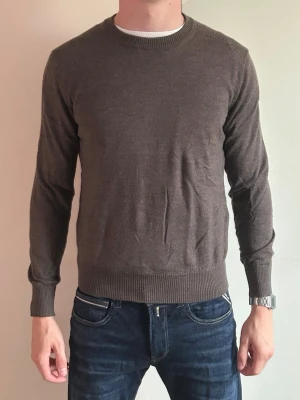 Brun stickad tröja från Asket - Säljer en stilren brun stickad tröja från Asket. Tröjan har rund halsringning, långa ärmar och ribbade muddar vid ärmslut och nederkant. Perfekt för lager-på-lager och passar till både jeans och chinos.