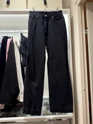 Svarta raka jeans med hög midja - Säljer ett par svarta jeans med rak passform och hög midja. Jeansen har klassiska fem fickor och knappgylf. Materialet är kraftig denim som ger en snygg och tidlös look. Perfekta till en avslappnad stil och passar till det mesta. Midjemått 31cm , från midja till skrev 28cm , innrebenslängd 65 cm