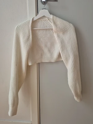 Vit ribbad bolero från SHEIN - Säljer en vit ribbad bolero från SHEIN i storlek XS. Den är stickad och har lång ärm samt croppad passform. Perfekt att slänga över ett linne eller klänning för en snygg lager-på-lager-look. Noppig och begagnad. Hund finns i hemmet.