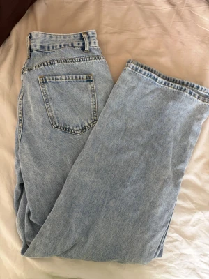 Ljusblå raka jeans med hög midja - Säljer ett par ljusblå jeans med rak passform och hög midja. Klassisk femficksmodell med dragkedja och knapp framtill. Jeansen har bälteshällor och är tillverkade i bomull för en skön och avslappnad look.
