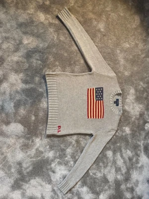 Polo Ralph Lauren Flag sweather  - Detta är den stickade flagg tröjan från polo Ralph Lauren. Den är i färgen grå och i storlek 10-12 år ca 140-152 cm. Den är både för killar och tjejer. Den är i sjukt bra kvalité! Den är absolut som en helt ny, har används fåtal gånger!