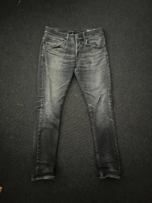 Svarta skinny jeans med slitningar - Säljer ett par svarta skinny jeans med snygga slitningar och tvättade detaljer. Jeansen har fem fickor, dragkedja och knapp i midjan samt coola dragkedjor på bakfickorna. Perfekta för en trendig och avslappnad stil.