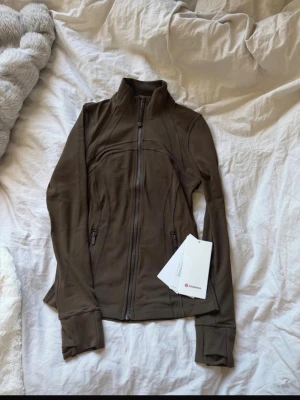Lululemon define jacket  - Snygg brun zip-jacka från Lululemon med hög krage och figurnära passform. Såklart äkta! 
