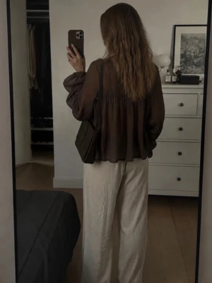 Brun transparent blus med volymärmar - Säljer en brun, transparent blus med voluminösa ärmar och v-ringning med knytband. Blusen har en lös och flowy passform, perfekt för lager på lager. Materialet är tunt och ger en luftig känsla. Passar dig som gillar en avslappnad men trendig stil.