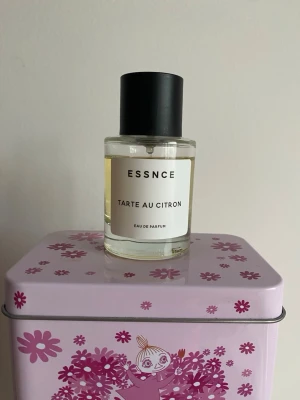 ESSNCE Tarte au Citron parfym - Fräsch parfym från ESSNCE med doften Tarte au Citron. Flaskan är cylindrisk i genomskinligt glas med svart rund kork och enkel vit etikett med svart text. Innehållet är ljusgult och ger en modern, minimalistisk känsla. Mängd enl bild. Har förvarats mörkt o svalt 