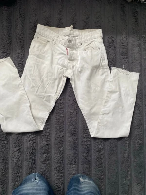 Vita jeans från Dsquared2 - Säljer ett par vita jeans från Dsquared2 med klassisk femficksmodell och rakt ben. Jeansen har råa, avklippta benslut och silverfärgade detaljer vid fickorna. Materialet är kraftigt denim i bomull. Perfekta för dig som gillar en clean och trendig look. Kan till och med tro att den är riktigt för alla märken och sådant är på byxorna! Byxorna passar mig bra och jag är runt 170cm lång
