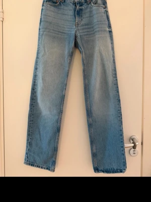 Ljusblå raka jeans med medelhög midja - Säljer ett par ljusblå jeans med rak passform och medel hög midja. Jeansen har klassisk femficksdesign och är tillverkade i ett kraftigare denimtyg. Perfekta för en avslappnad och trendig look.