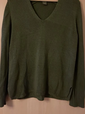 Olivgrön stickad tröja Lindex - Olivgrön stickad tröja från Lindex med v-ringning och långa ärmar. Tröjan har ribbade muddar vid ärmslut och nederkant. Perfekt för lager på lager och enkel att matcha med olika stilar.