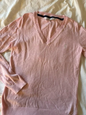 Ljusrosa stickad tröja Polo Club - Ljusrosa stickad tröja från Polo Club med v-ringning och lång ärm.  Perfekt för lager-på-lager och enkel att matcha med jeans eller kjol.