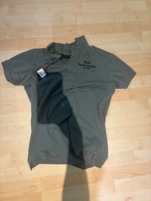 Grön Peak Performance t-shirt - Snygg grön t-shirt från Peak Performance med tryck på bröstet. Klassisk passform med korta ärmar och rund hals. Perfekt till jeans eller shorts för en avslappnad stil.