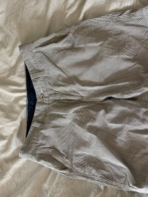 Randiga shorts i bomull - Snygga randiga shorts i vitt och grått med klassisk passform. Tillverkade i mjuk bomull med fickor både fram och bak samt bälteshällor. Perfekta för varma dagar och enkel att matcha med olika stilar.