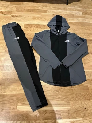 Grå och svart loungewear-set med huva - Snyggt loungewear-set The North Face i grått och svart. Setet består av en zip-hoodie med huva och texten 'ZERO-9' på ryggen samt matchande byxor med resår i 