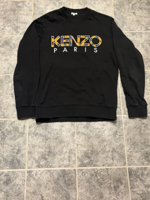 Kenzo Paris sweatshirt - Svart sweatshirt från Kenzo med stort färgglatt Kenzo Paris-tryck på bröstet. Tröjan har rund halsringning, långa ärmar och ribbade muddar vid ärmslut och nederkant. Perfekt för en trendig streetwear-look.