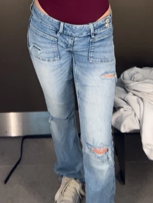 Ljusblå bootcut jeans low waist - Trendiga ljusblå jeans med bootcut-passform och slitningar på benen. Jeansen har dubbla knappar i midjan, framfickor med lock och en avslappnad vibe. Perfekta för en cool och avslappnad stil. Säljer pågrund av att jag inte använder dom plus dom börjar bli små för mig.❤️