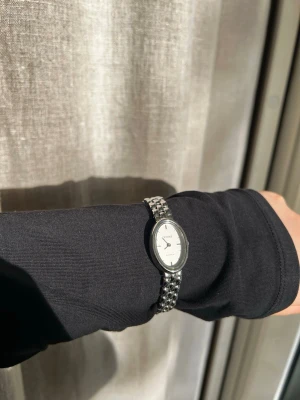 Silverfärgad oval klocka från Cendré  - Stilren klocka från Cendré (modell Phoebe) med oval urtavla i vitt och silverfärgat armband i metall. Klassisk design med minimalistisk look och tydliga svarta visare. Perfekt accessoar för dig som gillar enkel och tidlös stil. Ser exakt ut som ny, enbart använd fåtalet gånger. Nypris: 1800 kr