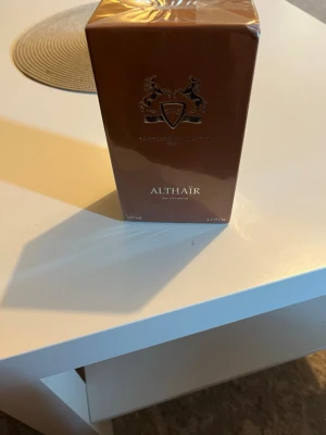 Parfums de Marly Althaïr Eau 125ml - Lyxig parfym i brun, glansig kartong från Parfums de Marly. Althaïr är en Eau de Parfum och flaskan rymmer 125 ml. Förpackningen har eleganta detaljer med guldtext och emblem. Perfekt för dig som gillar exklusiva dofter. Pris går att diskutera.