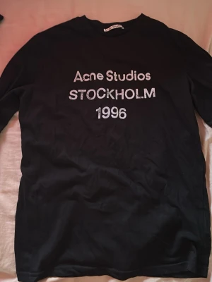 Svart långärmad Acne Studios t-shirt - Säljer en svart långärmad t-shirt från Acne Studios med trycket 'Acne Studios STOCKHOLM 1996' på bröstet. Klassisk passform och rund halsringning, perfekt för en clean och stilren look.