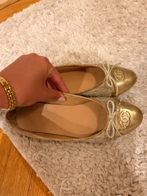 Guldiga ballerinaskor från Chanel - Säljer ett par ballerinaskor med guldiga tåpartier och vita rosetter. Jag hade de på min student 
