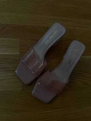 Rosa transparenta klackar  - Säljer ett par trendiga pumps i ljusrosa med transparent rem över foten och fyrkantig tå. Klacken är bred och genomskinlig vilket ger en modern vibe. Perfekta för dig som vill sticka ut med stilrena detaljer.