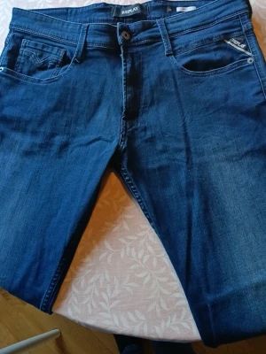 Mörkblå jeans från Replay - Snygga mörkblå jeans från Replay med klassisk femficksmodell och diskret Replay-logga på myntfickan. Jeansen har raka ben och är tillverkade i ett mjukt denimtyg som sitter skönt. Perfekta för dig som gillar stilrena och tidlösa jeans.