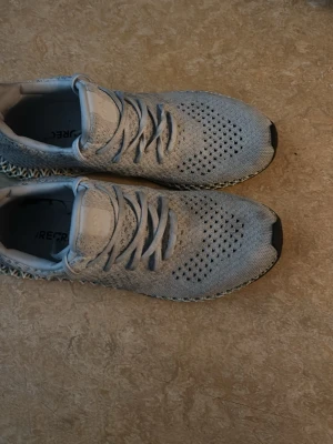 Ljusgrå sneakers med stickad ovandel - Snygga ljusgrå sneakers med stickad ovandel och ventilerande meshmönster. Skorna har en unik, 3D-printad sula i ljusgrönt och svart samt klassisk snörning. Perfekta för dig som gillar modern och sportig stil.Dom är också lite smutsiga annars har dom inga problem helt nya kostar runt 5000kr 