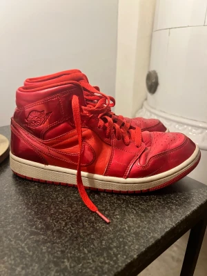 Röda Air Jordan 1 High sneakers - Snygga röda Air Jordan 1 High sneakers i läder med klassisk vinge-logga på sidan. Skorna har röda skosnören, vit sula och detaljer i olika röda nyanser. Perfekta för dig som vill sticka ut med en ikonisk och sportig stil. Sparsamt använda skick enligt bilderna 😊priset inte hugget i sten
