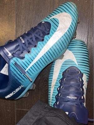 Nike Mercurial elite blå fotbollsskor - Säljer ett par Nike Mercurial fotbollsskor i blått med vita detaljer, skorna är sällsynta där av priset på 1000kr kan diskuteras