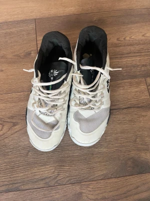 Vita Salming sneakers med svart logga - Säljer ett par vita sneakers från Salming med svart logga på sidan. Skorna har vita snören, meshdetaljer för ventilation och svarta partier på sulan. Lågt skaft och vadderad insida för extra komfort. Perfekta för en sportig och avslappnad stil.