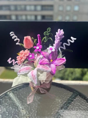 Blomsterarrangemang i piprensare - Unikt blomsterarrangemang i pastellfärger, gjort av piprensare och tyg. Innehåller rosa, lila och gröna blommor och blad, dekorerat med organzaband och placerat i en liten guldfärgad kruka. Perfekt som dekoration till skrivbord eller fönsterbräda.