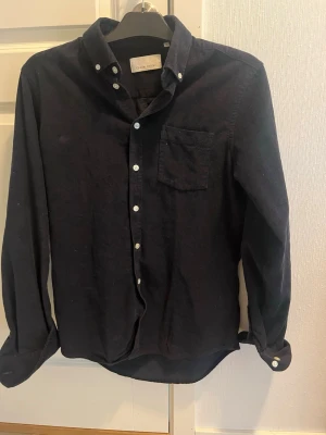 Mörkblå manchester skjorta Casual Friday - Säljer en mörkblå manchester skjorta från Casual Friday i storlek S. Skjortan har klassisk krage, bröstficka och vita knappar framtill samt på ärmsluten. Perfekt för dig som gillar en stilren och enkel look.