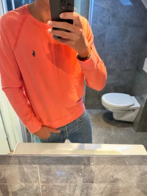 Korallfärgad tröja från Polo Ralph Lauren - Snygg korallfärgad långärmad tröja från Polo Ralph Lauren med rund halsringning och den klassiska mörkblå loggan broderad på bröstet. Tröjan är i riktigt bra skick och har inga skador. Jag på bilden är 188cm som referens. Hör av er vid vidare frågor;)