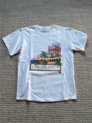 Vit t-shirt från Casablanca - Vit t-shirt från Casablanca med färgglatt tryck av byggnad och palmer på framsidan | Är i storlek S | Fraktas inom 1 dag