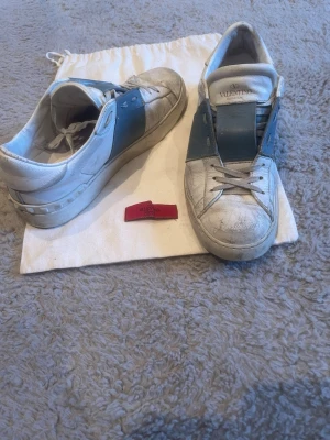 Valentino vita skor med blå detalj - Säljer ett par vita sneakers från Valentino med bred blå läderdetalj över sidan och ovandelen. Köpte dom för 4000 och har använt dom ganska mycket men har gjort rent dom och inget har gått sönder på skorna. Dustbag ingår när man köper skorna.