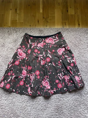 Midi, knälång kjol från Paul Smith mönstrad, lowwaist, lågmidjad - Supersöt kjol från Paul Smith i brun med rosa blommigt mönster. Sparsamt använd och i superfint skick enda ”skavanken” är att haken där man knäpper kjolen hade behövt sys fast lite (bild 2). Knäpps med dragkedja i sidan, 100% bomull och har även en underkjol dvs 2 lager tyg. Storleken är en L men funkar utmärkt till S om man vill ha den lågmidjad.   Midjemått: 39cm  Längd: 54cm