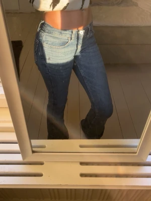 Blå bootcut jeans med broderade fickor - Säljer ett par klassiska lågmidjadd blå bootcut jeans med snygga broderade detaljer på bakfickorna. Jeansen har normal passform. Perfekta för dig som gillar en tidlös och avslappnad stil. Säljer dessa för att dom är på gränsen lite för korta för mig då jag är ganska lång ca 170 cm
