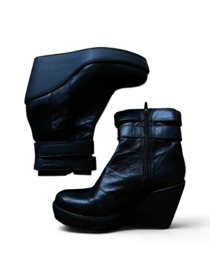 Svarta kilklackade stövletter i skinn - Snygga svarta vagabond stövletter med kilklack och dragkedja på sidan. Tillverkade i glansigt skinn med breda remmar upptill för en cool look. Notera slitningar på sidorna.