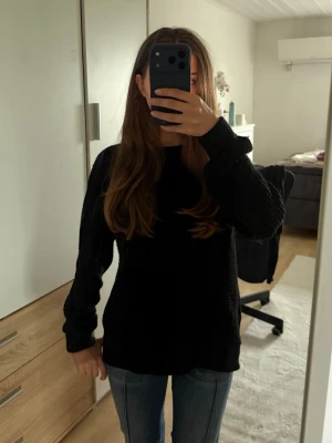 Svart stickad tröja  - En enkel och stilren svart stickad tröja med rund hals och långa ärmar. Tröjan har en rak passform och ribbade muddar vid ärmslut och nederkant. Perfekt att matcha med jeans för en avslappnad look.