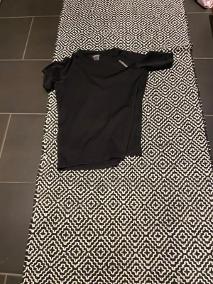Svart sportig t-shirt - En svart sportig t-shirt med korta ärmar och rund hals. Tillverkad i ett lätt och stretchigt material som passar perfekt för träning eller andra fysiska aktiviteter. Diskret logga på axeln ger en stilren look.
