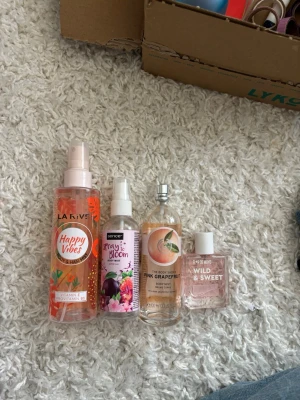 Fyra olika body mists och parfymer - Fyra fräscha body mists och parfymer: LA RIVE Happy Vibes i orange flaska, Sence Spray to Bloom i genomskinlig flaska med blommigt motiv, The Body Shop Pink Grapefruit i rund glasflaska och FAEM Wild & Sweet i liten rosa flaska. Perfekta för dig som gillar fruktiga och blommiga dofter.
