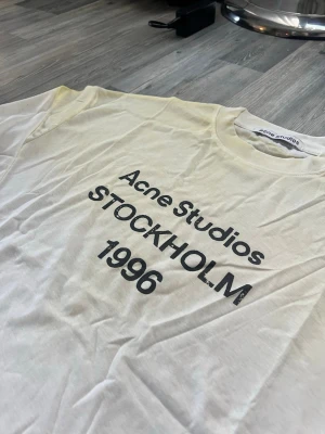 Acne studios tröja  - Säljer en vit långärmad topp från Acne Studios med tryck i svart text på bröstet: 'Acne Studios STOCKHOLM 1996'. Klassisk rund halsringning och relaxed fit. Perfekt för dig som gillar minimalistisk och stilren design.