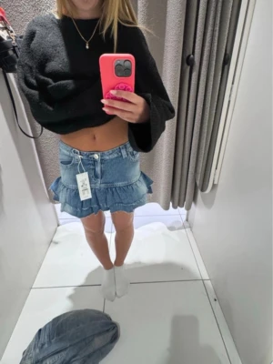 Blå jeanskjol med volang - Säljer en kort jeanskjol i blå denim med volangkant och råa kanter. Kjolen har fickor både fram och bak samt bälteshällor i midjan. Perfekt för dig som gillar en trendig och avslappnad stil.