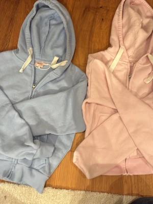Ljusrosa hoodie med dragkedja - 2 för 400! Mysig ljusrosa hoodie med dragkedja framtill och vit dragsko i huvan. Hoodien har ribbade muddar vid ärmslut och nederkant samt fickor på sidorna. Perfekt för en avslappnad och trendig look.
