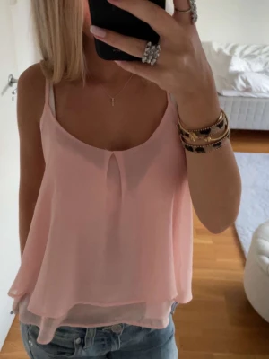 Ljusrosa topp - Säljer en ljusrosa, luftig linnetopp med omlott-look och tunn axelbandsdesign. Toppen har ett lager på lager-utseende och en liten öppning framtill vid halsen. 