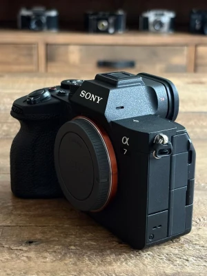 Sony α7iv systemkamera svart - Snygg och modern systemkamera från Sony, modell α7. Kameran är svart med greppvänlig struktur och har en robust, kantig design i metall och plast. Perfekt för dig som vill ta riktigt proffsiga bilder och gillar spegellösa kameror.